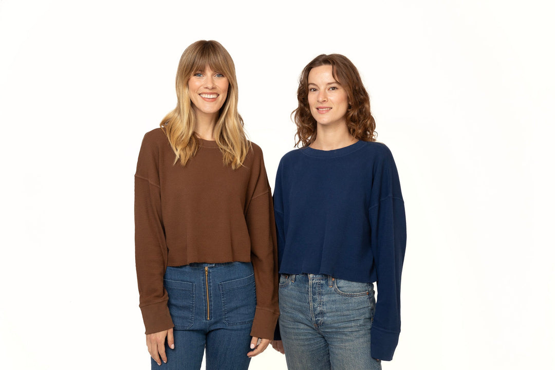 Two women wearing brown and blue sweaters with jeans on a white background